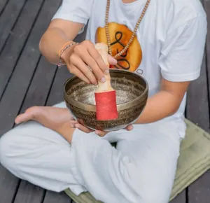 Hands playing a brass singing bowl with a red mallet during sound healing on a wooden deck in Canggu, Bali
