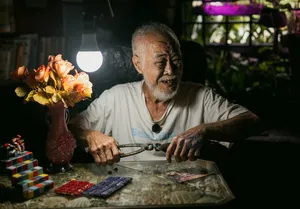 Lelaki meneliti kertas dan objek di atas meja dalam bilik bercahaya lembut, untuk kisah apartmen sewa Hidden Heritage dan permata tersembunyi Singapura