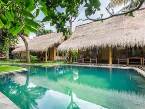 Thatched-roof villas and turquoise pool at Omunity Bali retreat in Bali, set for a sacred meditation and cleansing stay