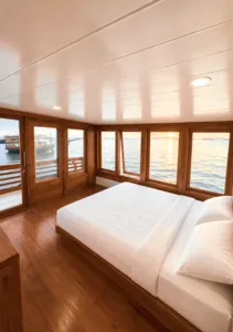 White-mattress bed in a wooden phinisi cabin with floor-to-ceiling windows, part of a 3D2N shared Komodo cruise from Labuan Bajo
