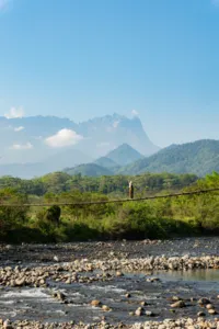 Hiker standing on a lookout above a river with a mountain horizon during a Borneo Overland Sabah road trip with Mt Kinabalu