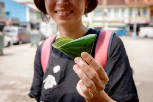 Seorang wanita tersenyum memegang daun hijau di jalanan Jalan Besar, diambil saat tur jalan kaki Hidden Heritage di Singapura — hidden gems Singapura