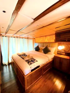 Cozy deluxe phinisi cabin in Labuan Bajo with neatly made bed, curtained window and warm wooden interiors for Komodo Island