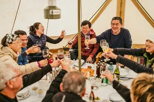 Group dining and toasting in a canvas dining tent during a nomadic caravan camp in Shangri-La’s remote valleys