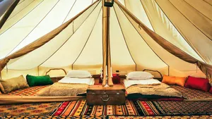 Cozy camp bed inside a canvas tent in Shangri-La’s remote valleys, neatly made with pillows, rugs and a bedside lantern