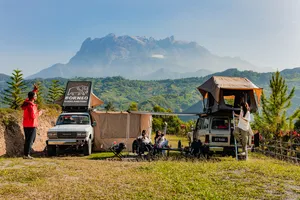 Borneo Overland wild camping base with canvas tents and parked 4x4s, with rolling Sabah valley views, Mt Kinabalu
