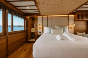 Travass Life new phinisi double cabin with a made bed, warm lighting and an ocean view through the window on a Komodo Island trip