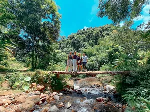 Walkers pause on rocks beside a shallow stream in the Lombok jungle during the Lombok Forest Tour forest walk