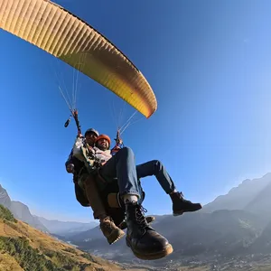 Paragliding tandem riders cradled beneath the amber canopy against the blue sky over mountain valleys, Sapa