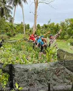 Travellers posing in the greenery of Kebun Lidstari permaculture farmstay, Langkawi, with raised garden beds and palms nearby