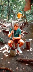 Participant kneeling by a forest fire during the Lombok former loggers walk, preparing a drink at a cooking setup