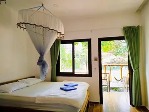Green Hope Lodge room with four-poster canopy bed, green curtains, and terrace view of trees at Cat Tien, 2D1N stay