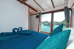 Phinisi cabin corner with neatly made beds and sea view through the windows on a private 3D2N Komodo cruise to Komodo Island