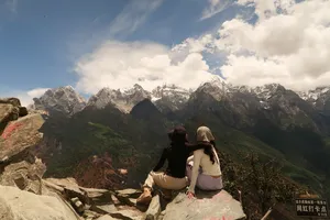 Two hikers sitting together on a viewpoint ledge, gazing at rugged snow mountains over Tiger Leaping Gorge, Lijiang, 2D1N high trail