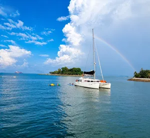 Zen Sea sailboat at sea near Singapore island shoreline, with a rainbow and kayaks in the calm water
