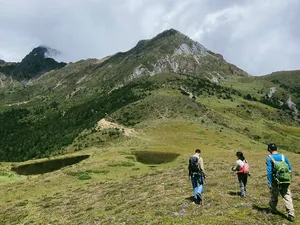 Small group hiking with backpacks on Jade Dragon Snow Mountain near Lijiang, overlooking a green valley and peak