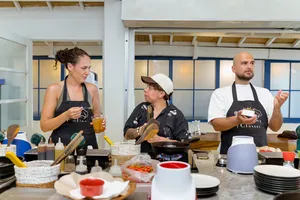 Gili Islands cooking class in Lombok: participants sip drinks and cook at cooking stations, sharing peanut-sauce flavours