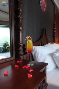 Cocktail with a flower garnish on a bedside table beside rose petals in a luxe Cat Ba cruise cabin by Sunshine Golden Cruises