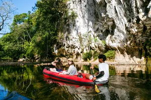 People relaxing in a red boat on Cheow Lan Lake, paddling past limestone cliffs at Khao Sok