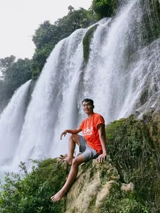 Solo traveller sitting on a grassy cliff beside a waterfall in Cao Bang on a Ha Giang Expeditions motorbike loop