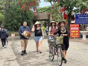 Travellers walking and cycling through Duong Lam ancient village near Hanoi, with red lanterns overhead and roadside signs