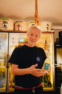 Host SakeMama welcoming guests at a rare sake tasting in Singapore, standing by a cabinet of bottles and labels