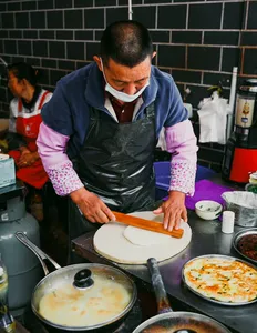 Local cook presses dough on a griddle for a Lijiang food hunt with local stories, in a Yunnan back-kitchen