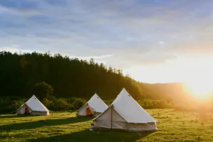Canvas tents pitched in a grassy meadow in Shangri-La’s remote valleys, glowing at sunset with forested hills behind