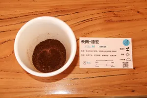 Close-up of a cup of dark coffee grounds beside a Yunnan tasting label card at Seeker Yunnan Coffee Estate in Lijiang