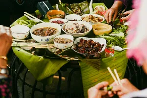 Santap bersama di Xishuangbanna dengan banyak hidangan tersaji di atas daun pisang, tangan-tangan menyiapkan dan menyajikan herba kepada para tamu