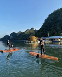 兰卡威丹绒鲁,高脚屋与丛林山丘旁的平静水面上,立式桨板玩家带着桨板前行
