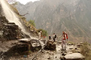 Hikers on the Tiger Leaping Gorge high trail in Lijiang, wading along a rocky route beside a roaring waterfall