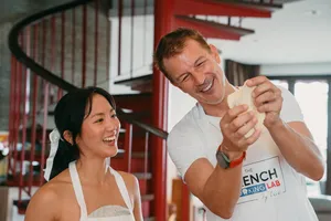 French chef showing croissant technique with a smiling participant in a Singapore cooking studio, both holding dough pieces