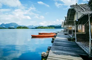 Wooden rafthouse jetty with moored orange kayaks on Cheow Lan Lake, viewed from the water at Khao Sok Riverside Cottages