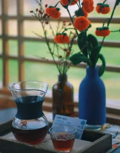 Glass pour-over brewer with two cups of Yunnan coffee on a wooden table, plus blue flower vase, at Seeker Yunnan Coffee Estate in Lijiang