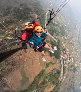 Smiling paraglider passenger in a helmet glides high above green hills and river valleys with gear visible in Sapa