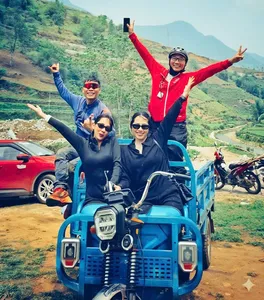 Group cheering while riding a blue open jeep on a scenic dirt road through green hills during a paragliding trip in Sapa