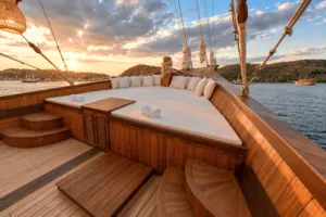 Sunset on a phinisi deck with cushioned lounge benches, railing steps and harbour views across the water in Labuan Bajo