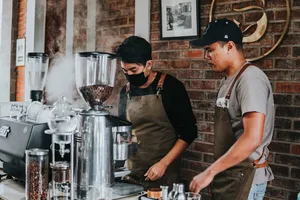 Bali Beans staff preparing coffee with espresso machine steam and grinders on a counter during a workshop in Bali.