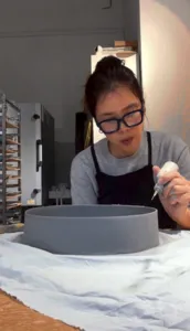 Potter from Ina Atelier shaping a small ceramic bowl over a grey plate on a workshop table during workshops in Singapore