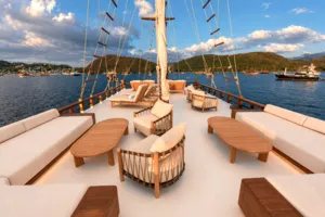 Komodo Island phinisi sundeck with beige daybeds and wooden tables, sail rig overhead on a Travass Life shared cruise