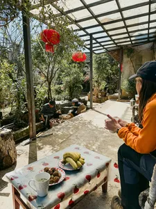 Orange-jacketed traveller reaching for food at a table in a shaded guesthouse courtyard in Lijiang during the village trek