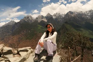 Traveller sitting on a mountain viewpoint with dramatic peaks and cloud breaks above Tiger Leaping Gorge, Lijiang on the hike