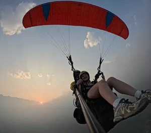 Silhouetted paragliding rider with a red canopy at golden hour, overlooking valley scenery from above the clouds in Sapa