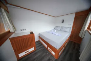 Wooden boat cabin with a neatly made bed and bedside chair for a solo-friendly 3D2N Komodo trip, Travass Life Labuan Bajo