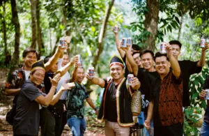 Sekumpulan jiran dan pengembara tersenyum sambil mengangkat minuman di ruang luar Ngapuh Homestead di hutan hujan Kuching