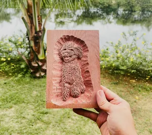 在会安户外,一只手拿着一尊雕刻木狮,背景是郁郁葱葱的花园景致