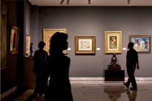 Silhouetted visitors stroll past framed artworks on an expert-led Vietnamese art tour at Quang San Art Museum in Ho Chi Minh City