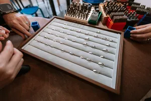Open wooden display tray filled with silver ring bands as hands choose pieces at Fat Anvil Studios in Singapore couple ring workshop