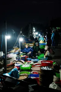 Vendors preparing food and supplies at a night-time market during a dawn Hoi An motorbike trades tour